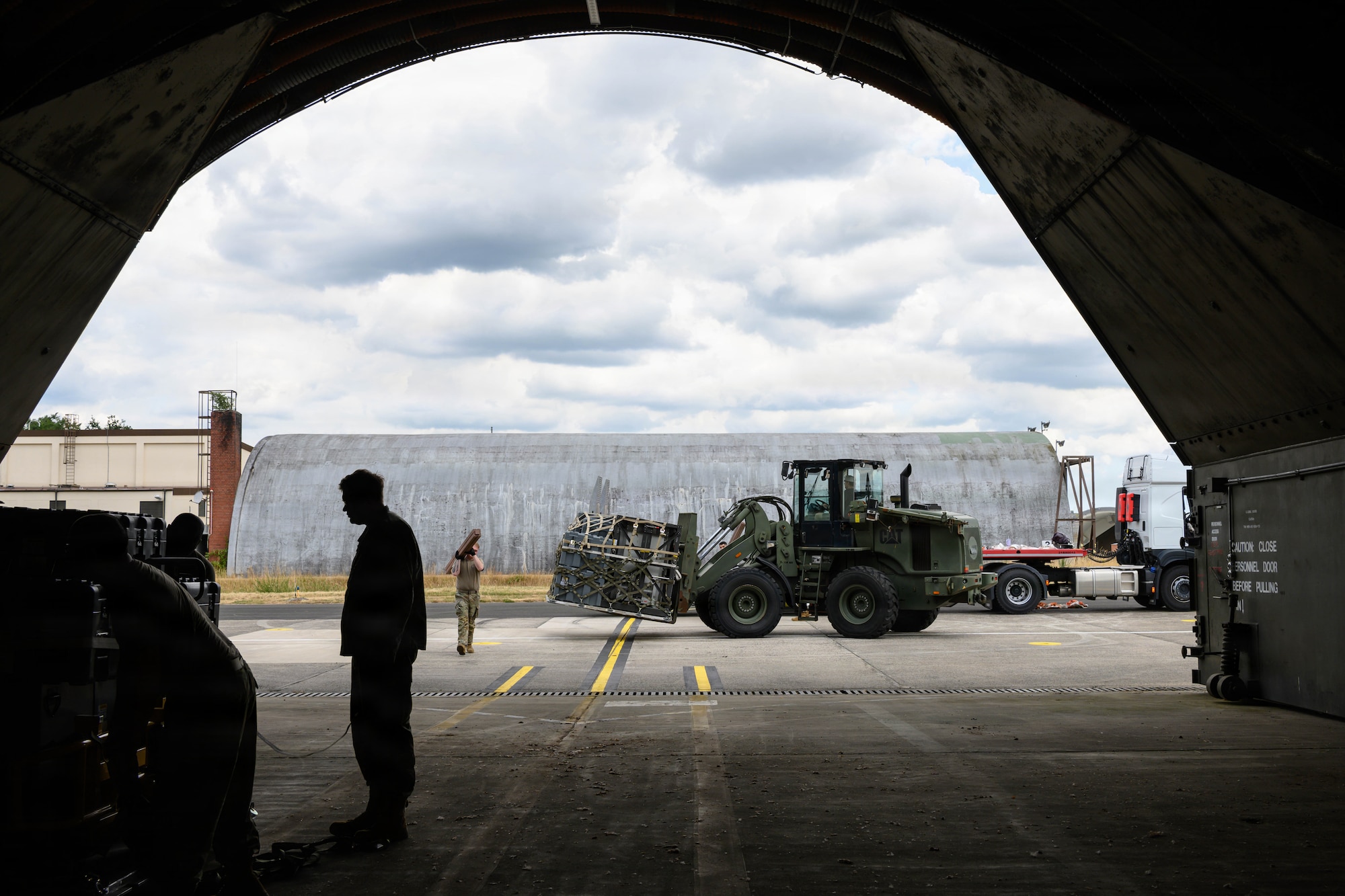A forklift holds a pallet outside of an aircraft shelter.