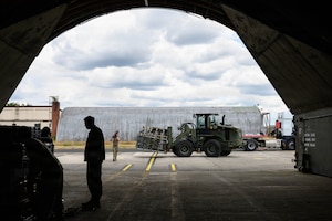 A forklift holds a pallet outside of an aircraft shelter.