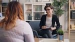 Therapist sits, holding a notepad, while listening to a patient.
