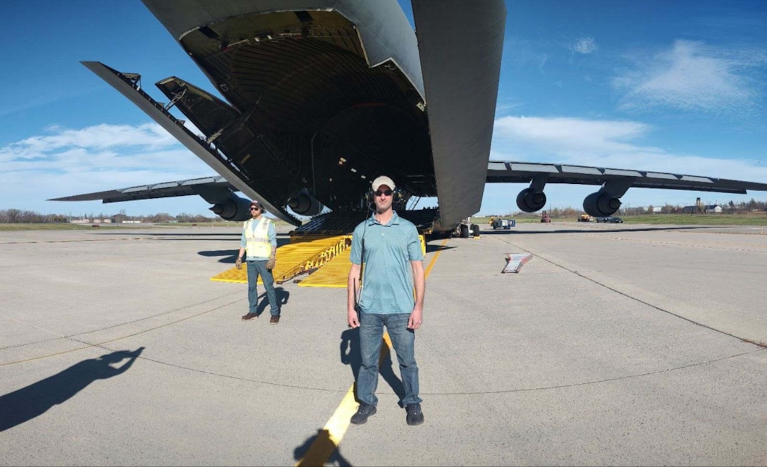 A man wearing blue jeans and a blue shirt stand near an aircraft
