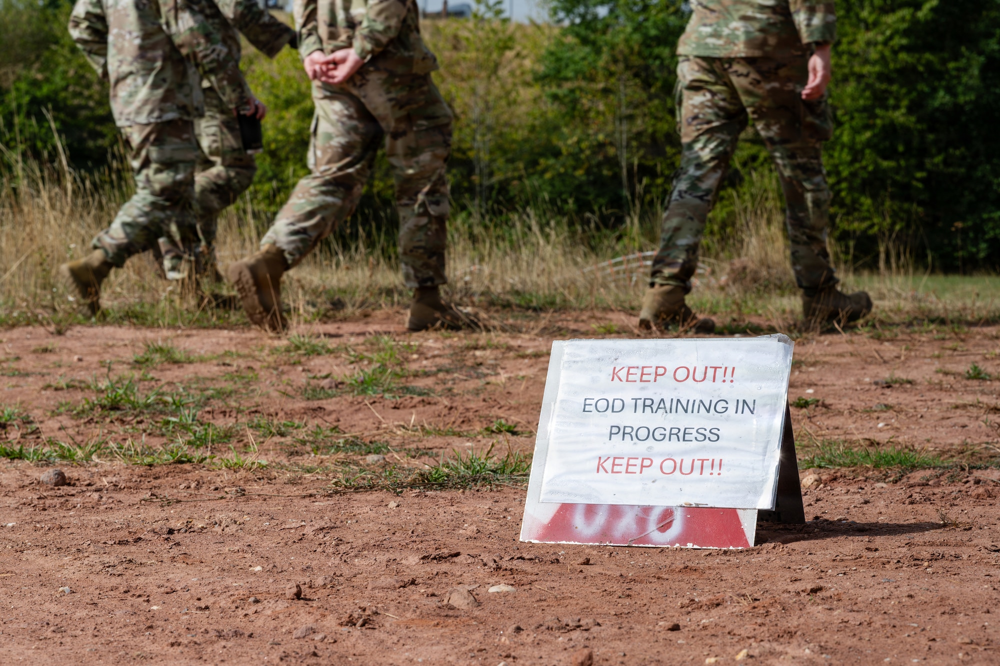 A sign on the ground reads: 
KEEP OUT!!
EOD TRAINING IN
PROGRESS
KEEP OUT!!