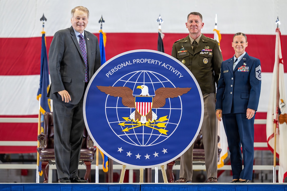 From left, Brian D. Birdwell, assistant secretary of War for sustainment; U.S. Army Maj. Gen. Lance G. Curtis, commander of the Personal Property Activity; and U.S. Air Force Chief Master Sgt. Karissa Gunter, senior enlisted leader of the Personal Property Activity, unveil the organization's new logo during an activation ceremony at Scott Air Force Base, Illinois, Sept. 9, 2026. The logo features six stars, representing the six service branches the activity serves.