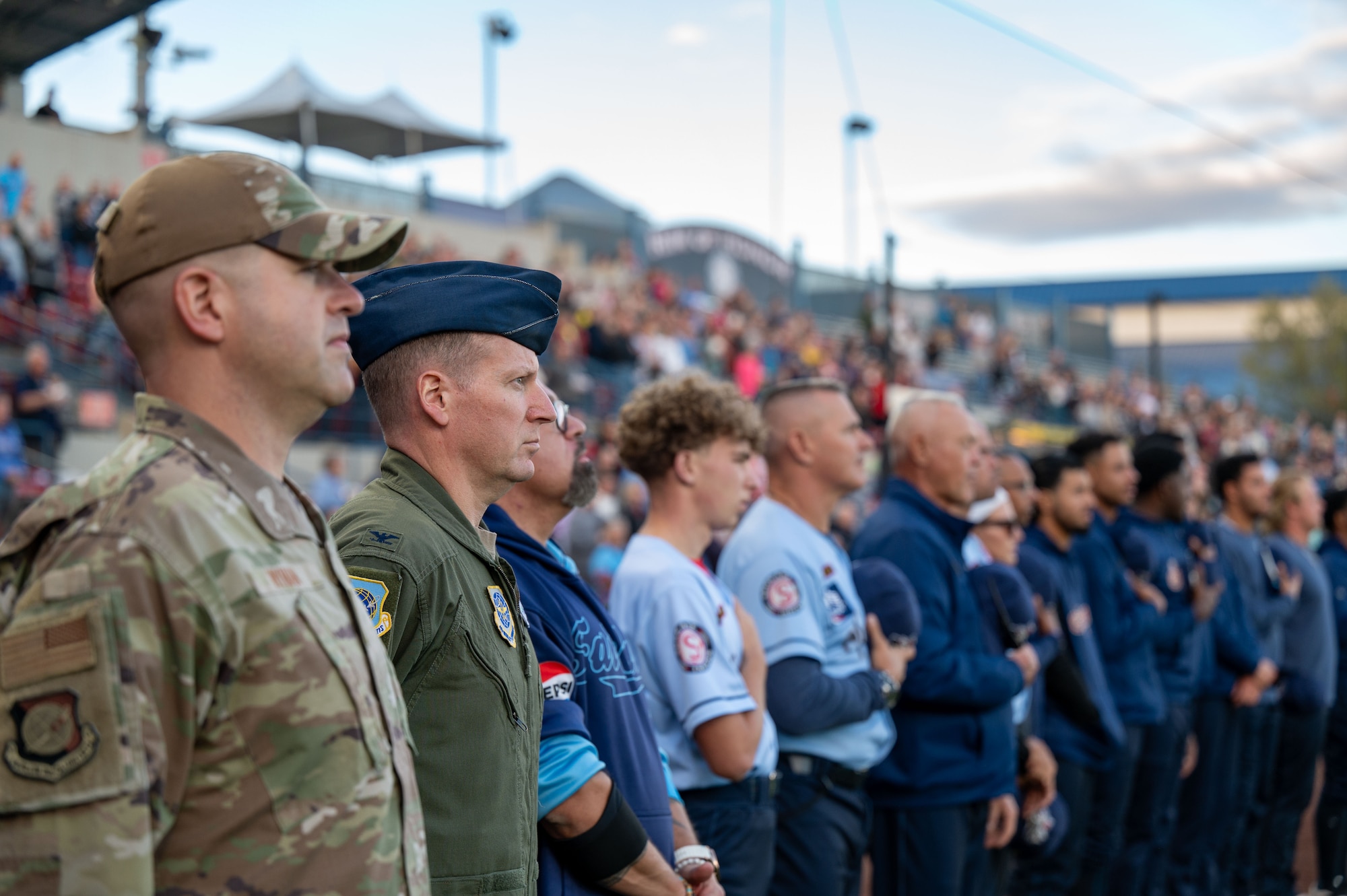 Members of Team Fairchild and the Spokane Indians baseball team listen to the national anthem.