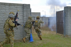 Uniformed men run around a corner with rifles during training.
