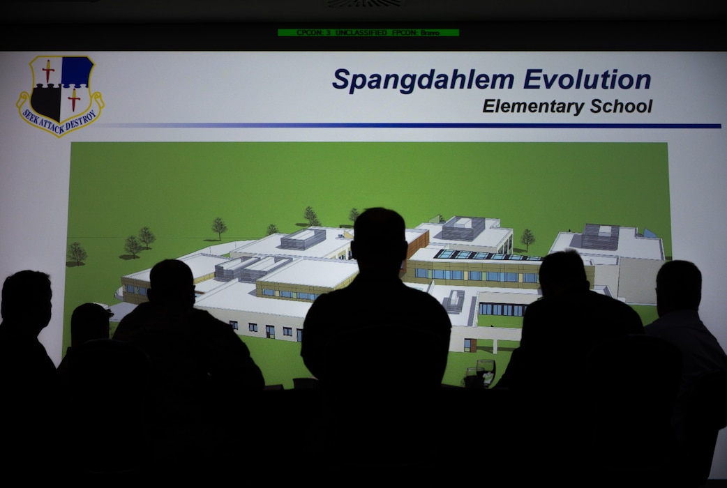 Silhouette of a group of people before a presentation slide titled "Spangdahlem Evolution, Elementary School".