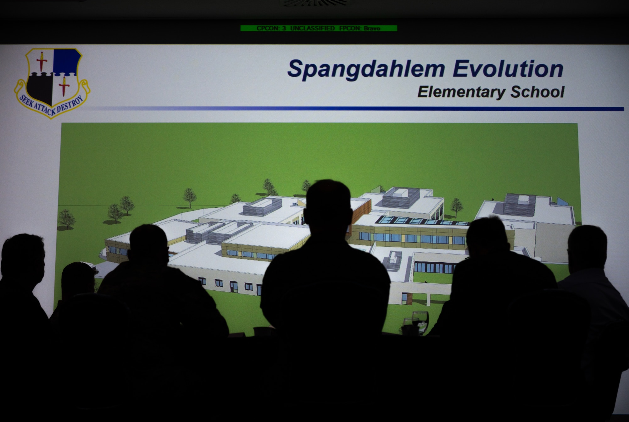 Silhouette of a group of people before a presentation slide titled "Spangdahlem Evolution, Elementary School".
