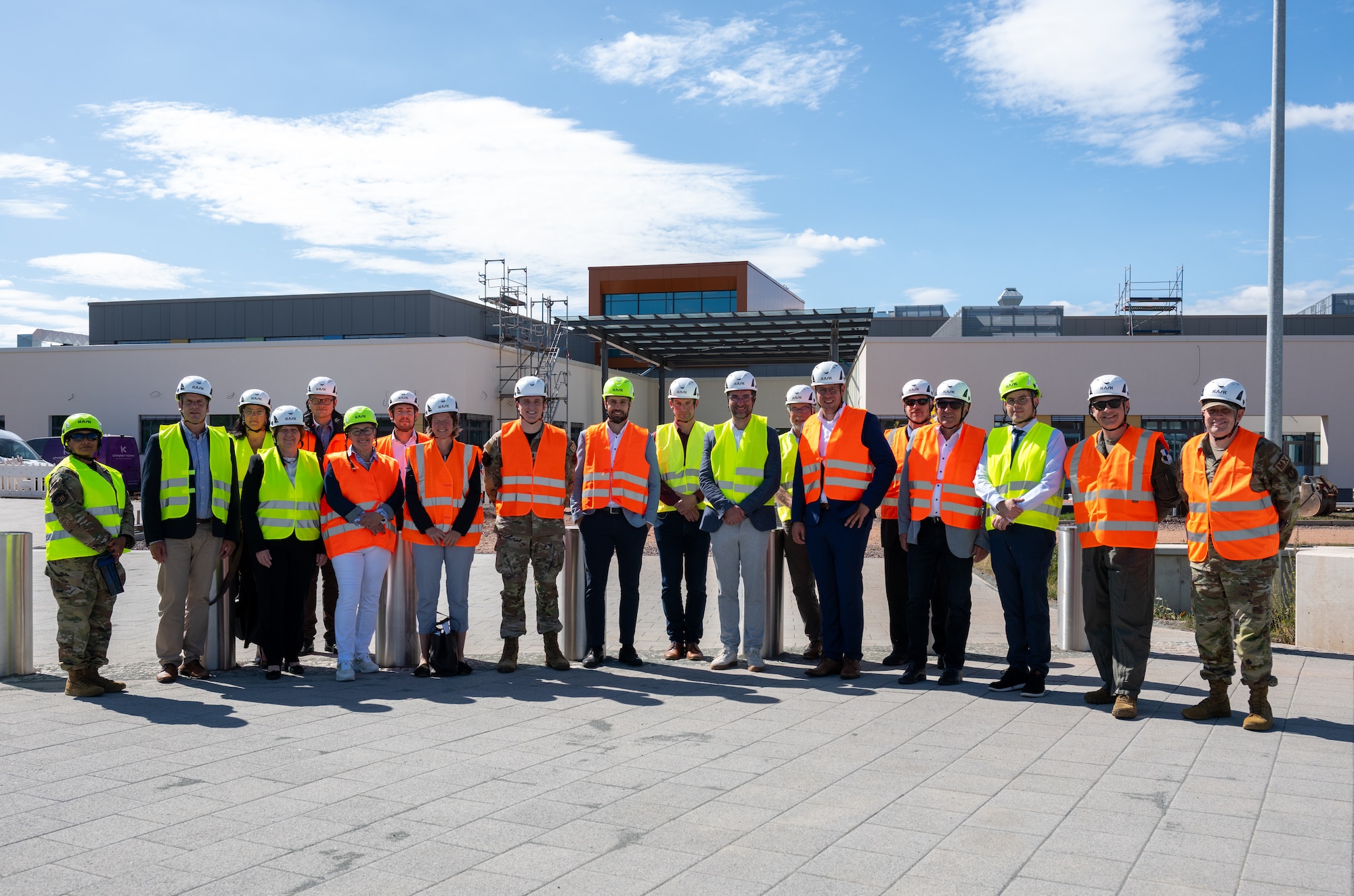 A large group of people wearing safety vests and helmets pose for a photo outside of a school building.