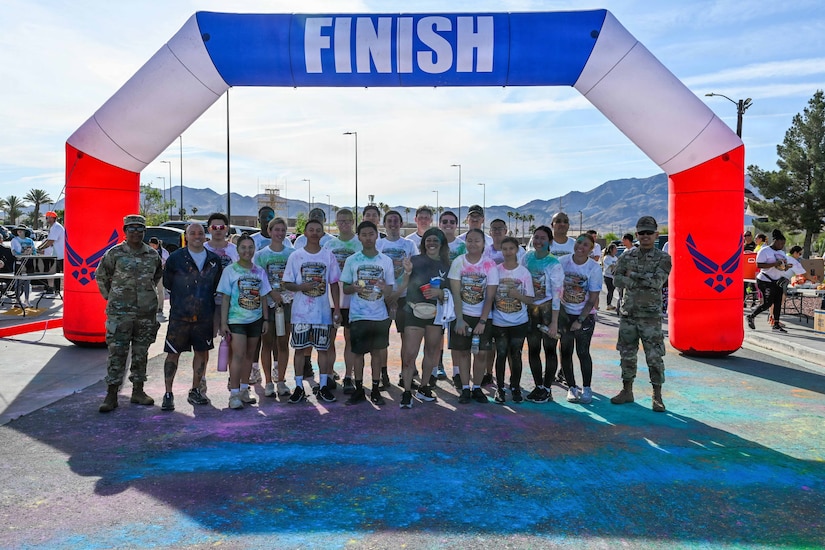 Nearly two dozen people in athletic attire and two people in camouflage military uniforms gather for a group photo under an inflatable arch that says, "Finish."