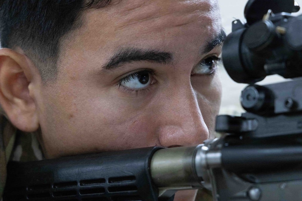 A soldier, in a zoomed view, aligns the rifle's sights.