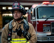 A man in firefighter gear stands in front of a fire truck.