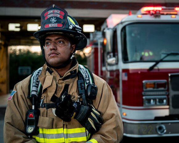 A man in firefighter gear stands in front of a fire truck.