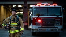 A man in firefighter gear stands in front of a fire truck.