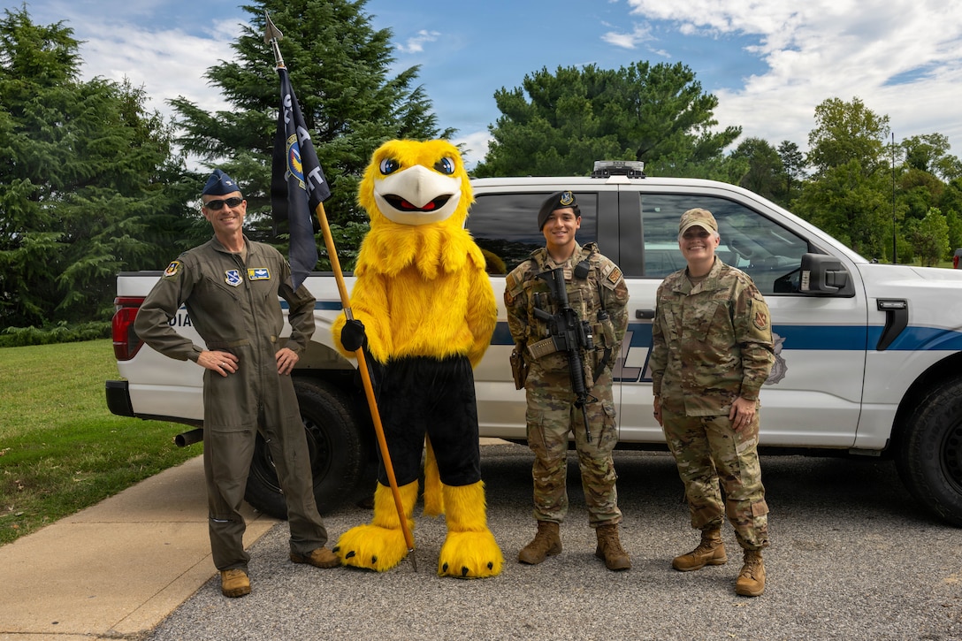 Service members pose with a mascot and flag in front of a military police vehicle.