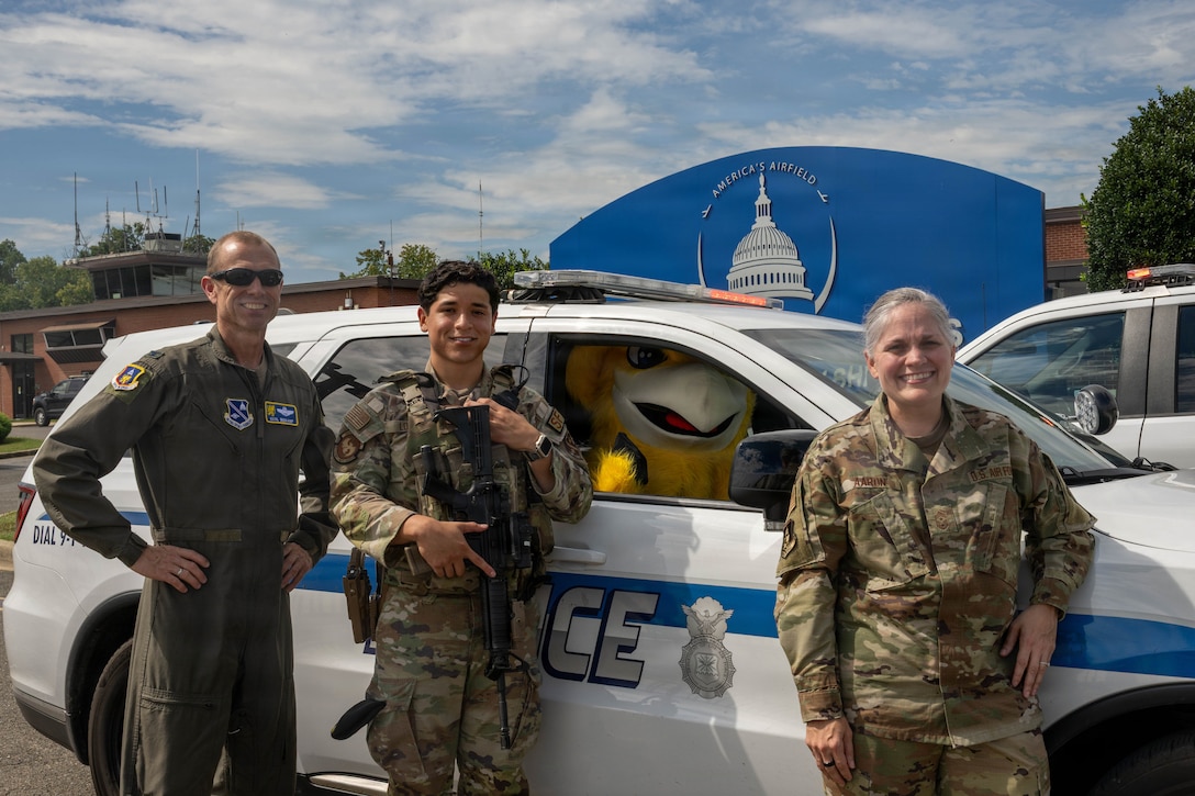 Service members pose with a mascot in front of a military police vehicle.