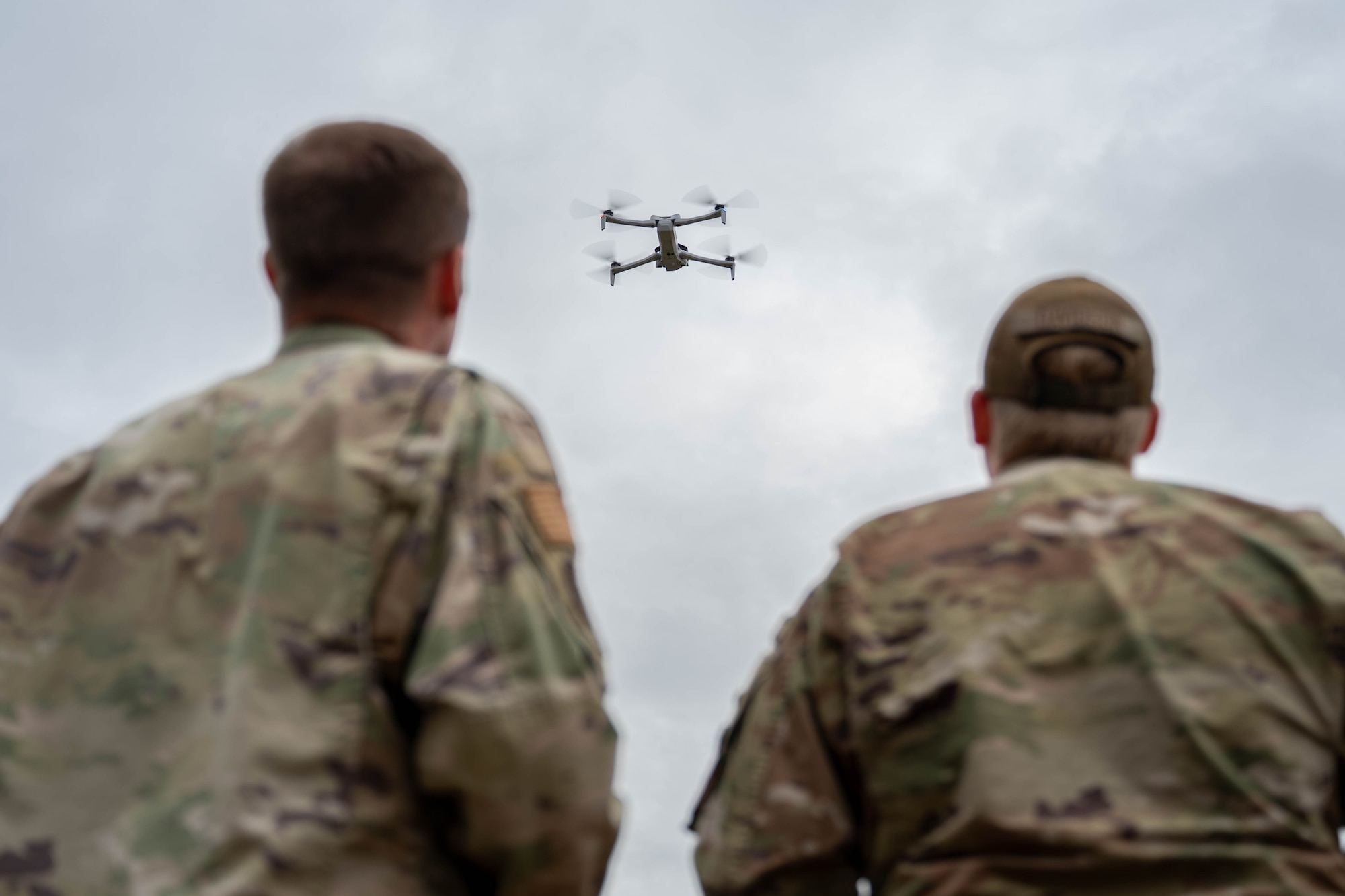 Two men look up at a hovering drone.