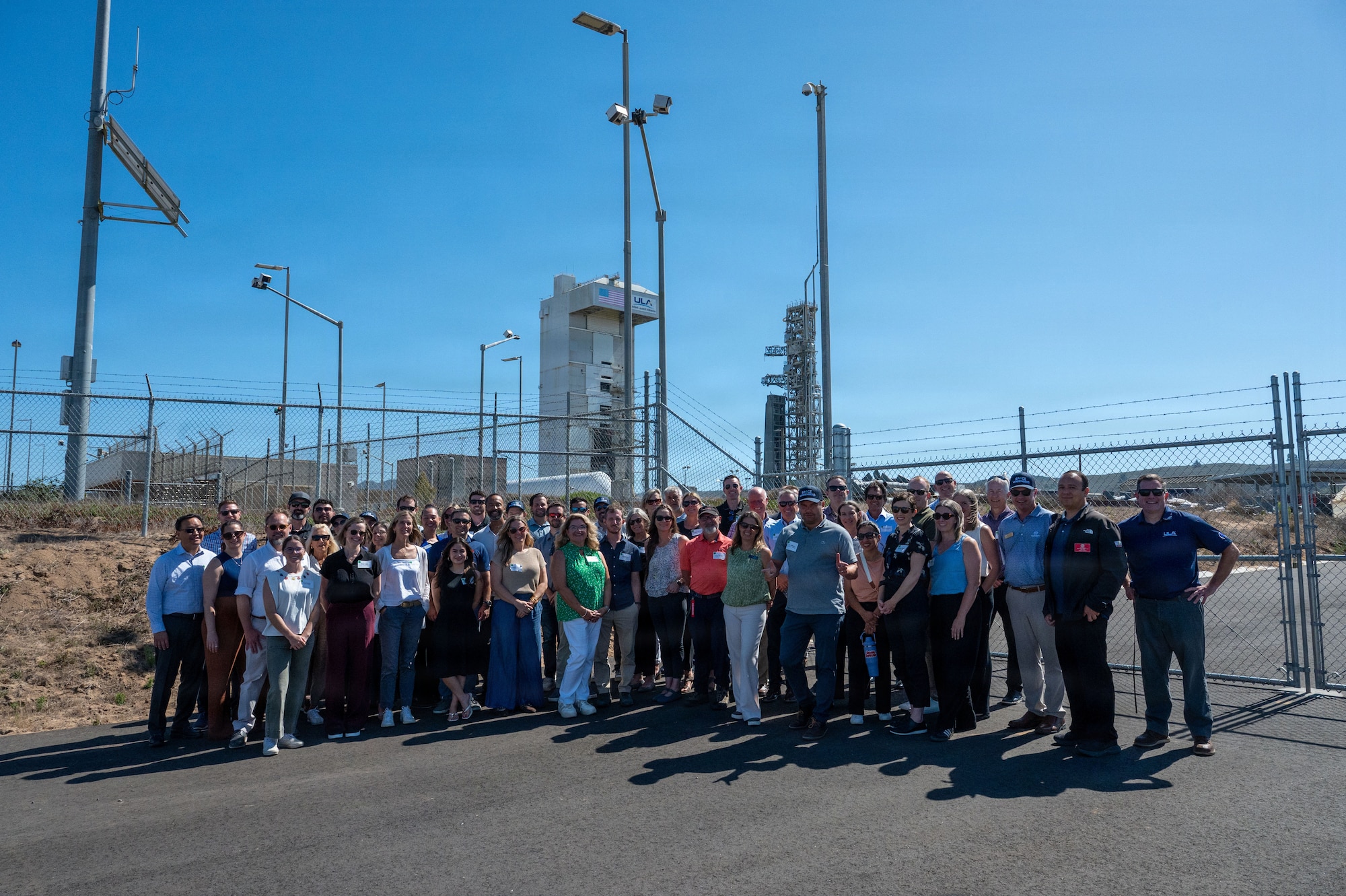 a group of people gather for a photo outside the fence around a space launch complex