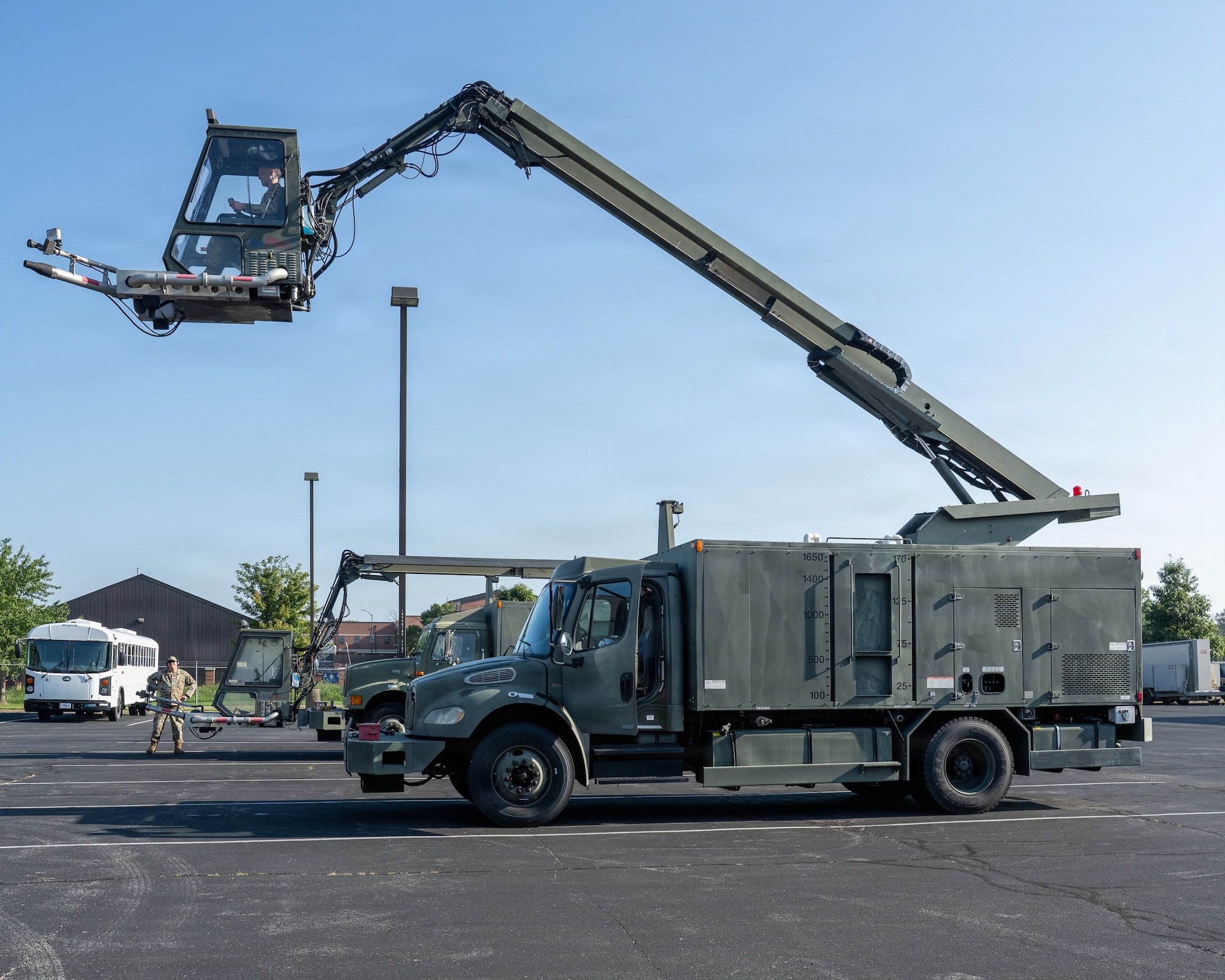 The cab of a deicer extended from a truck on the ground in a parking lot with an Airman inside.