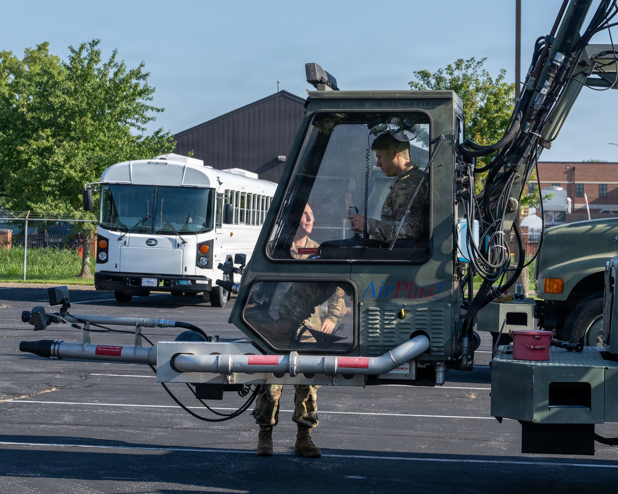 The cab of a deicer extended from a truck just a few feet off the ground in a parking lot with an Airman inside and another on the ground giving directions.