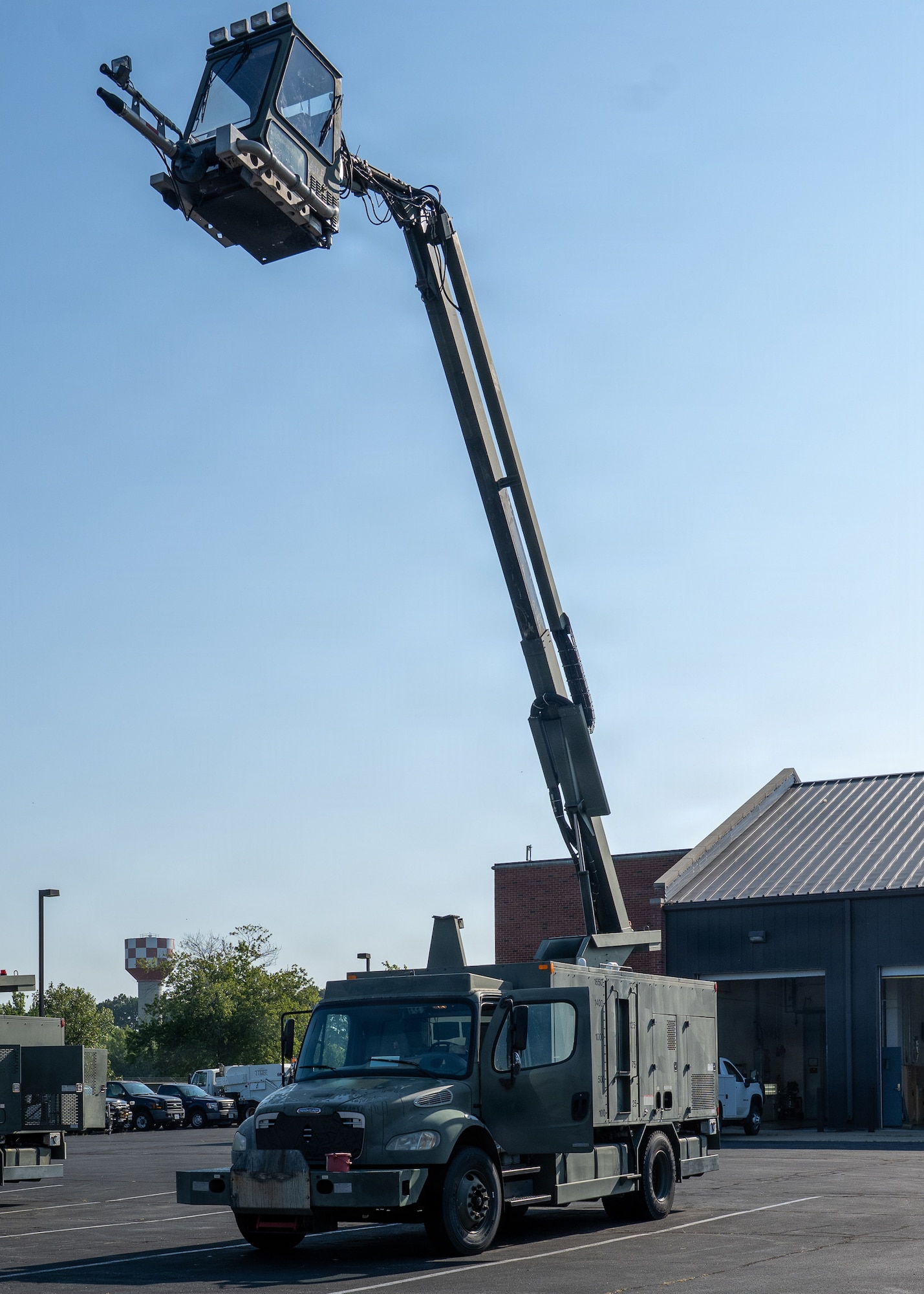 The cab of a deicer extended from a truck on the ground in a parking lot with an Airman inside.
