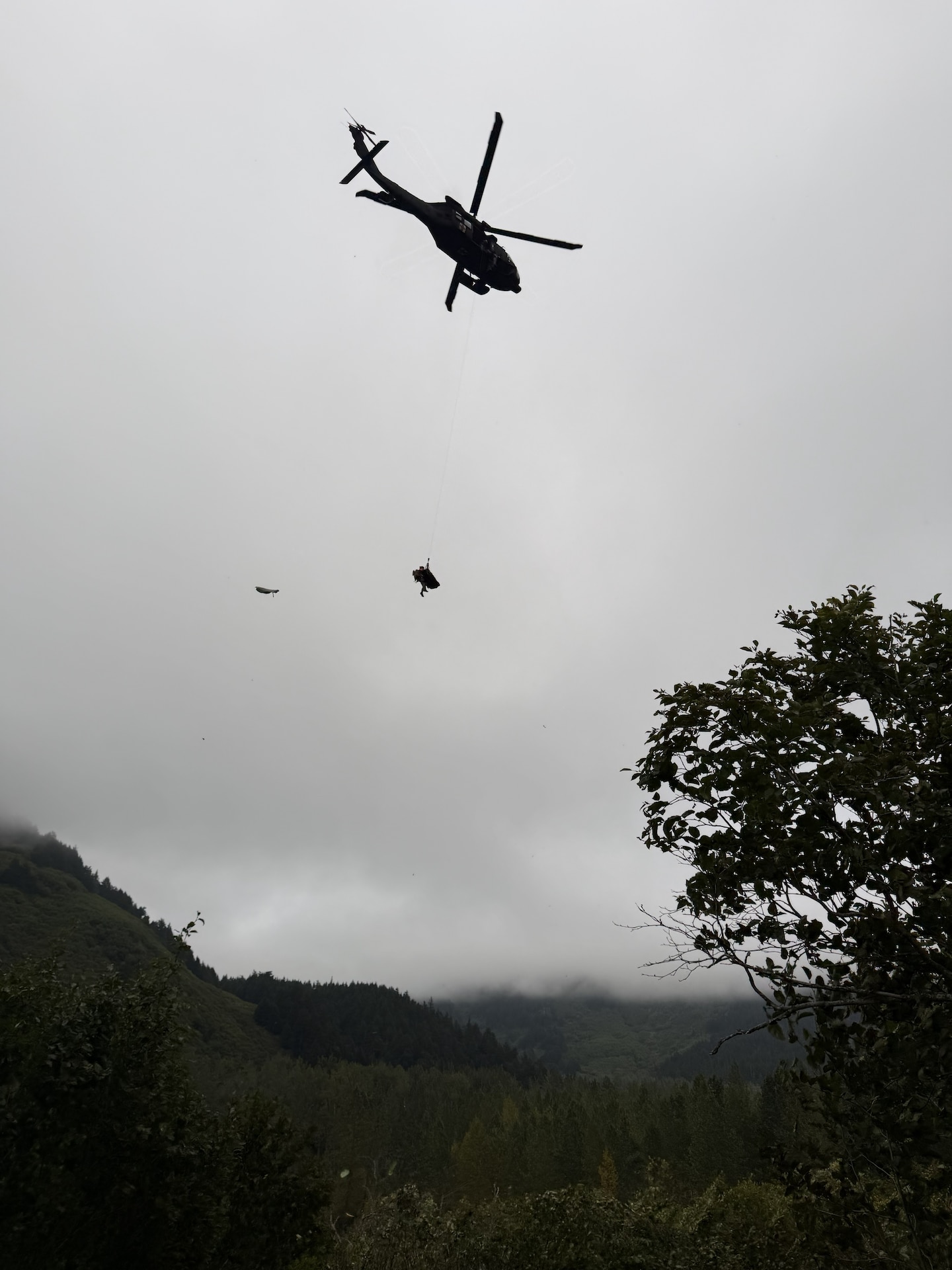 laska Army National Guard Staff Sgt. Steven Gildersleeve, critical care flight medic assigned to G Company, 2nd Battalion, 211th General Support Aviation Battalion, rides the hoist with an injured mountain biker in a litter during a rescue along the Winner Creek Trail near Girdwood, Alaska, Sept. 13, 2026.
