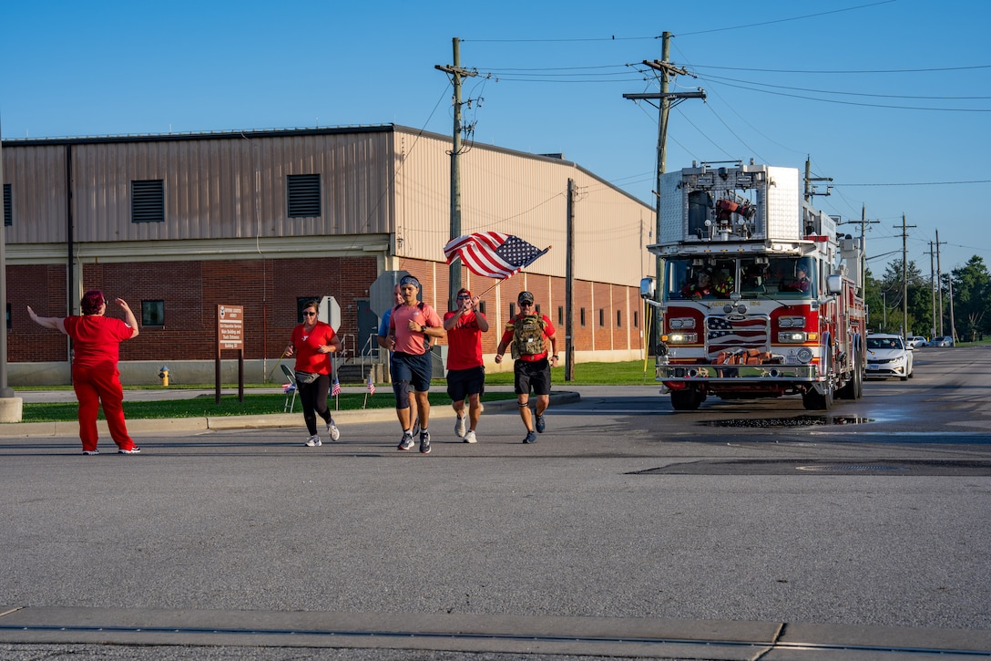 Several runners, one waving American flag, with fire truck following behind.