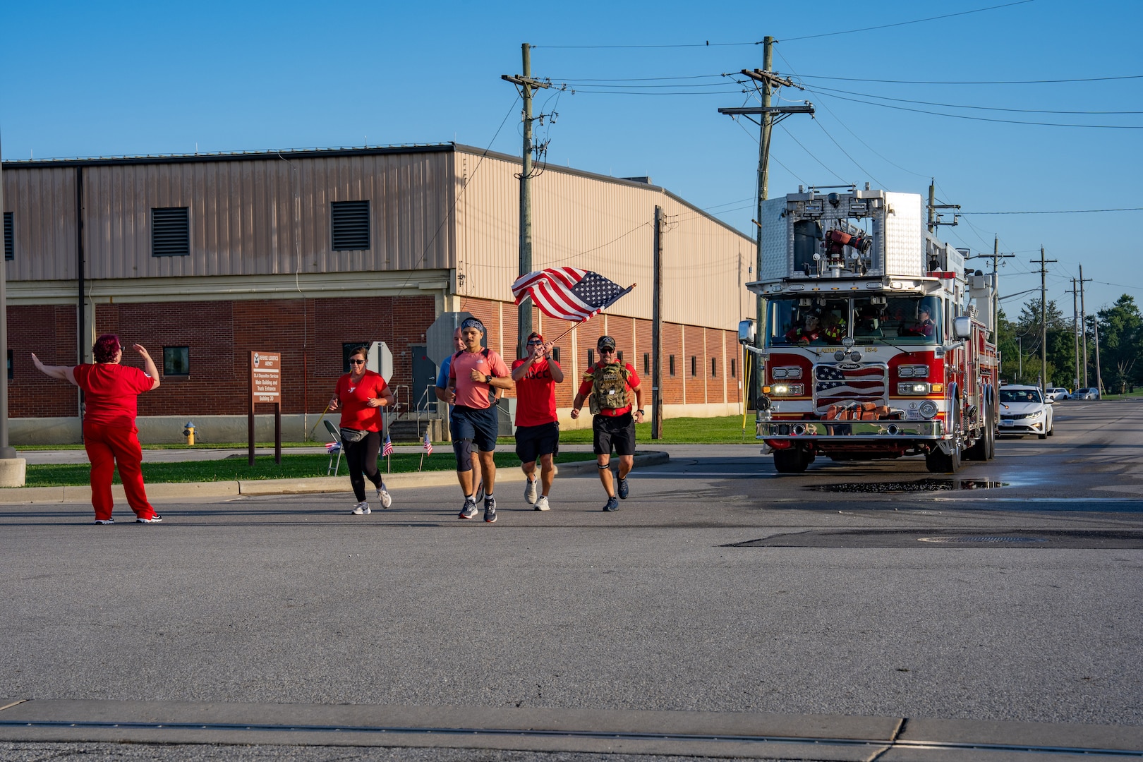 Several runners, one waving American flag, with fire truck following behind.