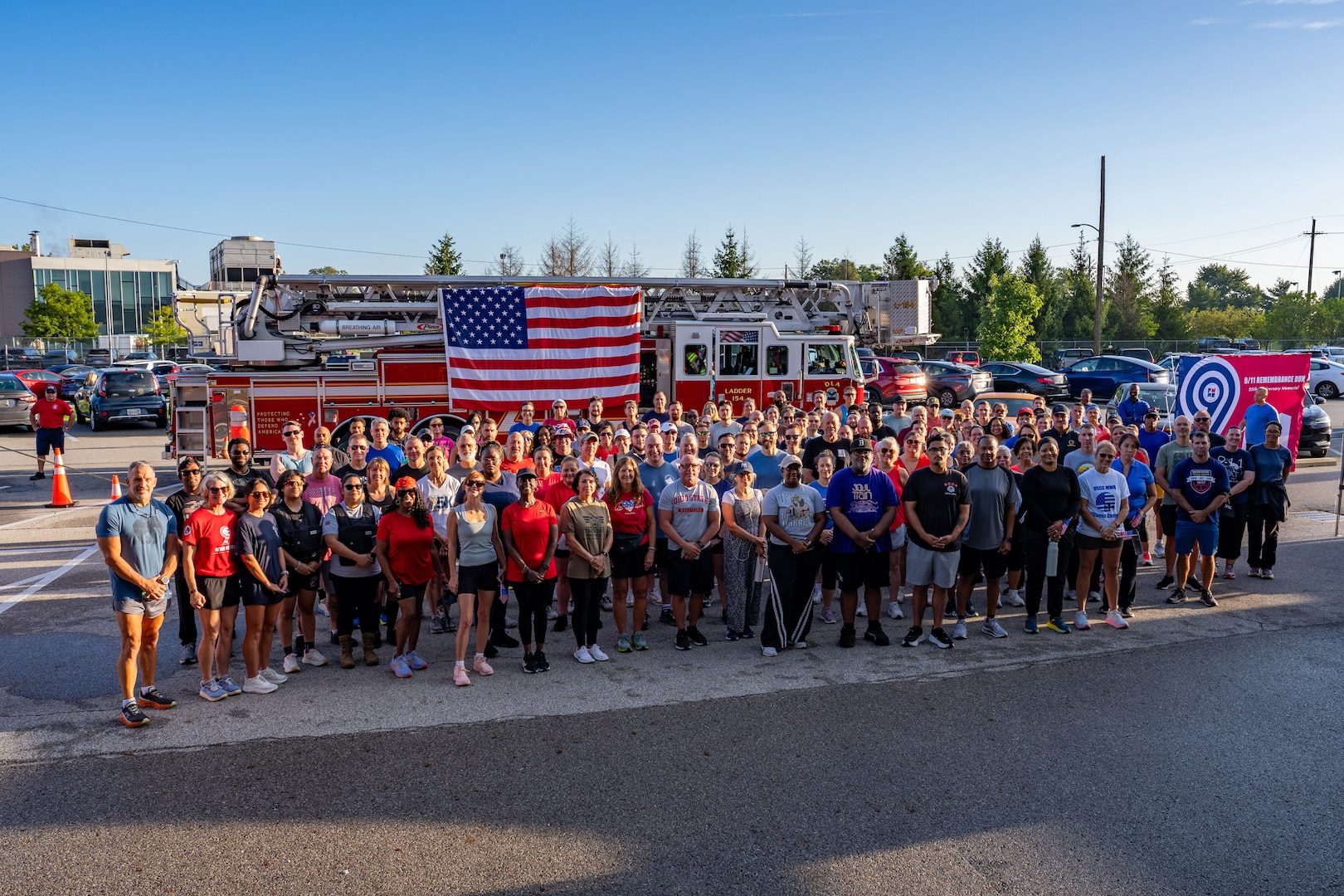 Large group poses for photo in front of firetruck with American flag hanging on the side.