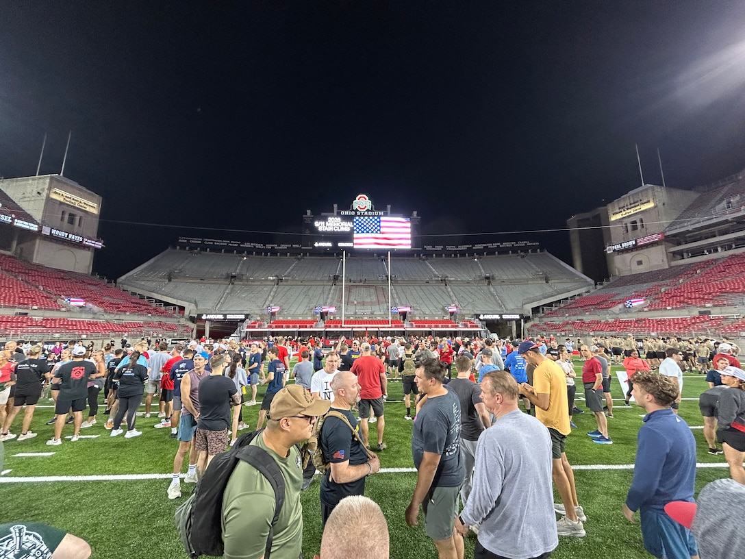 Lots of people  standing and chatting across football field - sky is black/dark