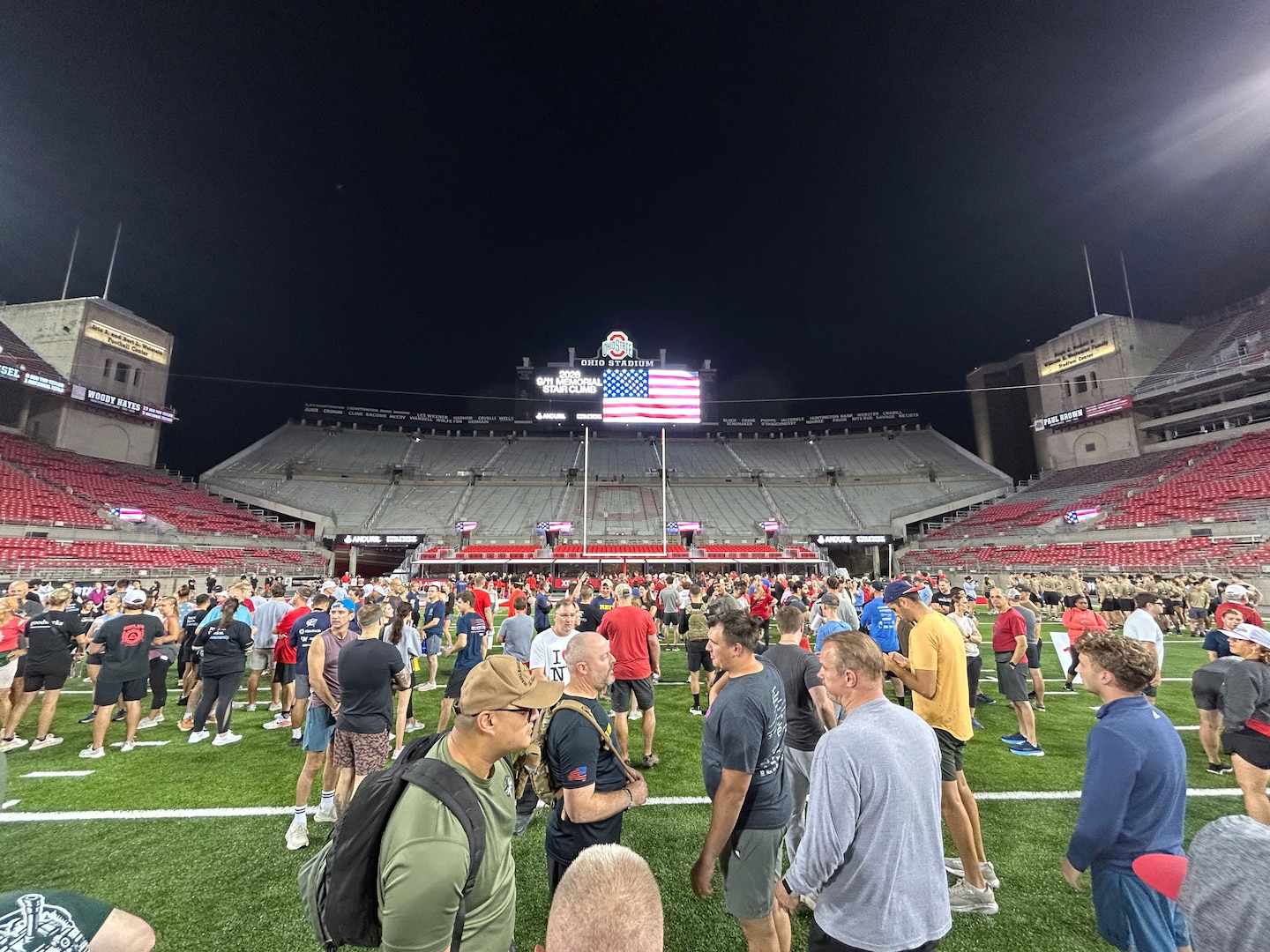 Lots of people  standing and chatting across football field - sky is black/dark