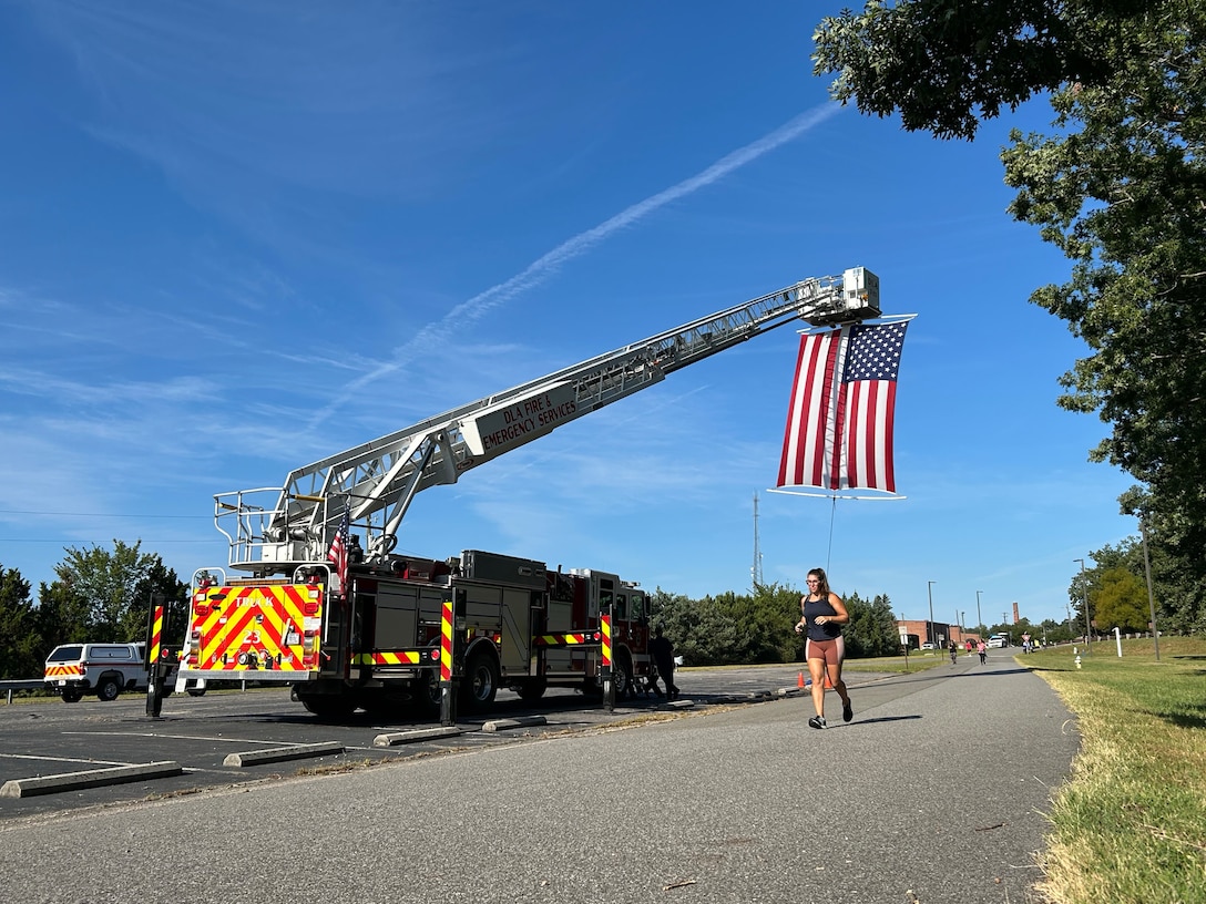 Woman running on pavement. Firetruck parked with ladder extended and American flag hanging