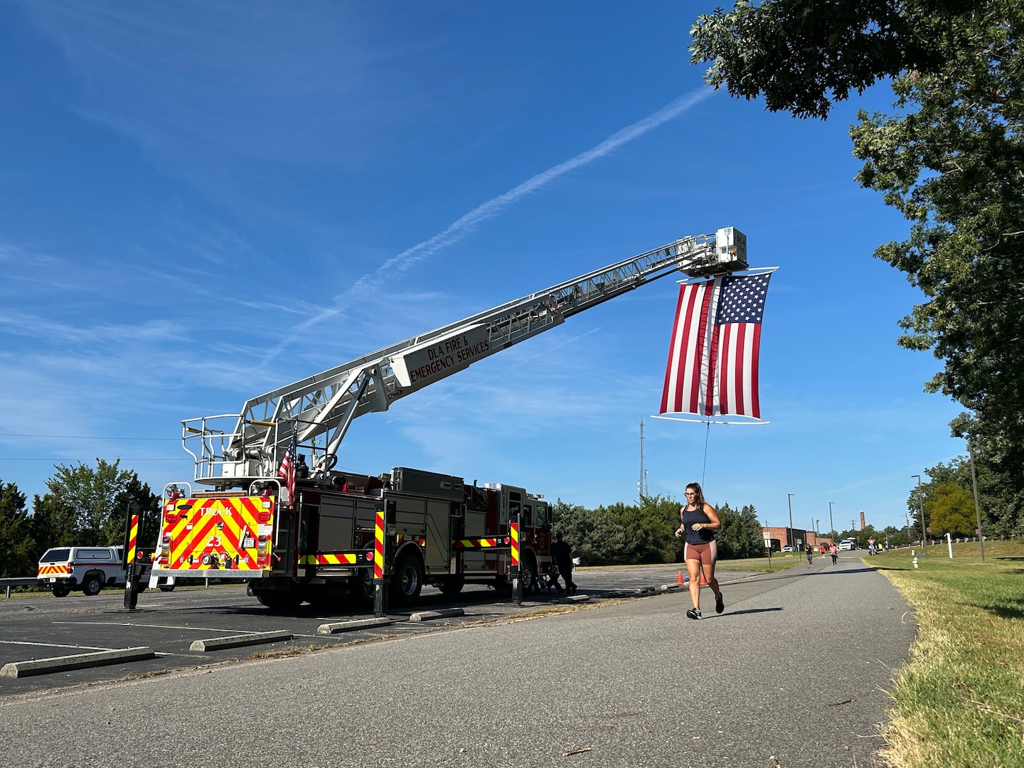 Woman running on pavement. Firetruck parked with ladder extended and American flag hanging
