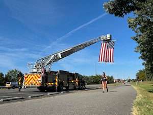 Woman running on pavement. Firetruck parked with ladder extended and American flag hanging