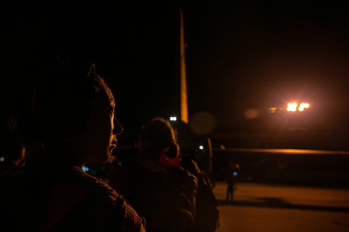 Service member stands in the dark next to a plane