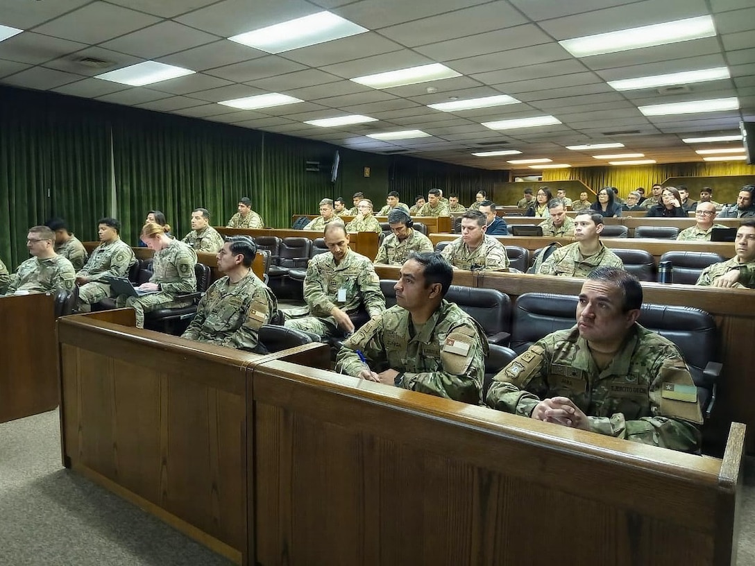 U.S. Army Soldiers and Chilean Army personnel sit and listen to a speaker not in frame.