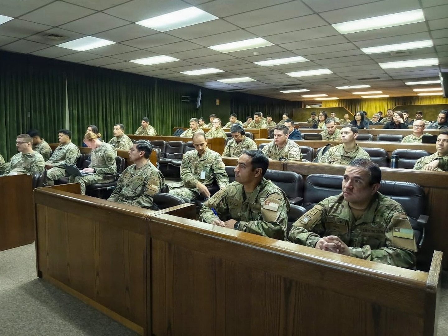 U.S. Army Soldiers and Chilean Army personnel sit and listen to a speaker not in frame.