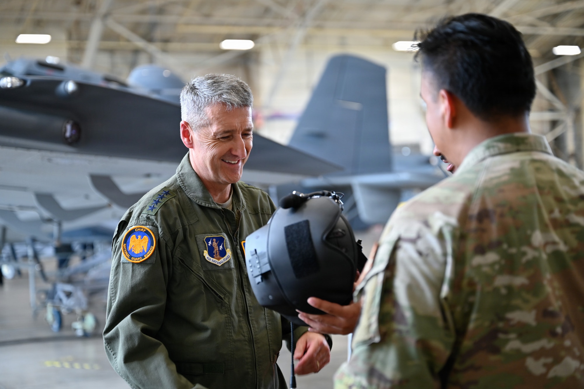 a man in a flight suit looks at a helmet