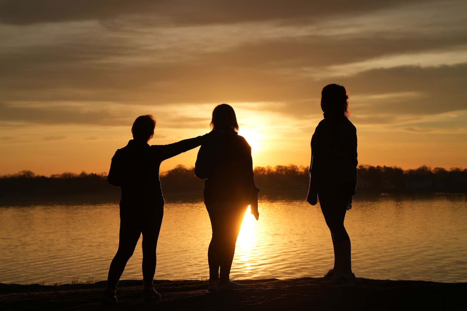Three silhouettes standing in front of water and a sunset
