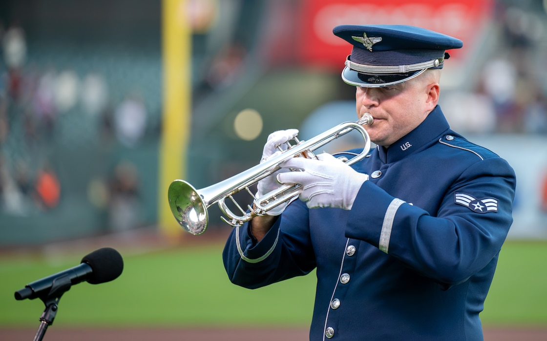 Airman plays trumpet before baseball game.