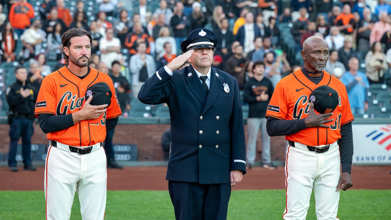 Baseball coaches and firefighter salute during baseball game.
