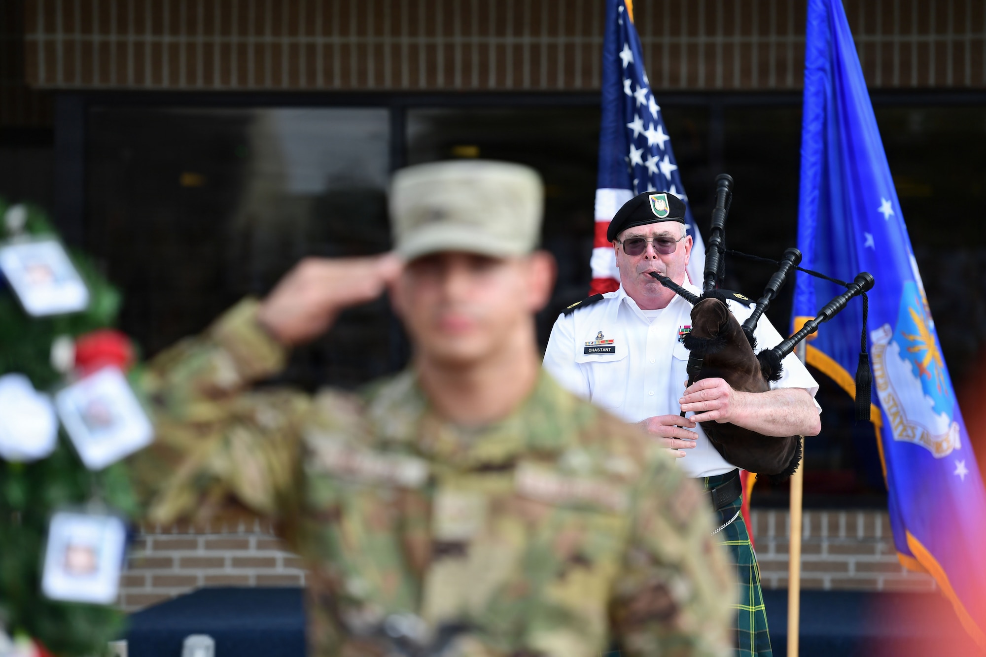 A man plays bag pipes while a U.S. Airman renders a salute in the foreground.