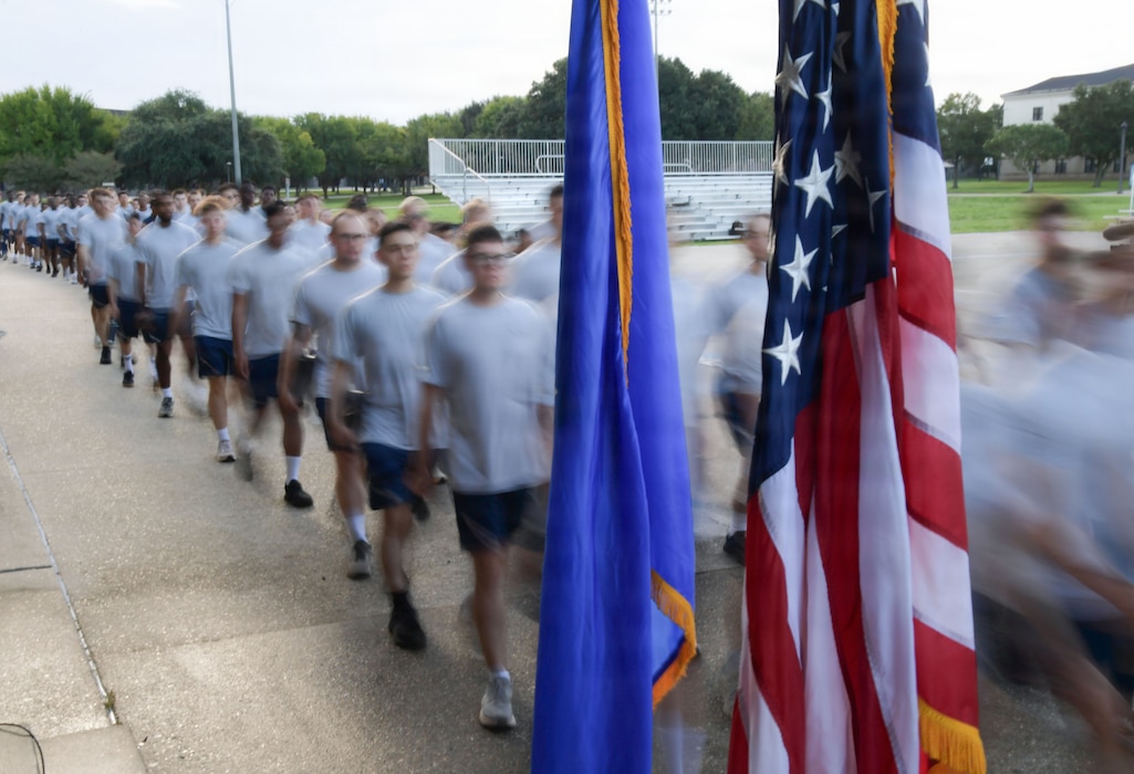 U.S. Airmen march by a U.S. flag and an Air Force flag.