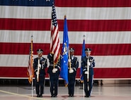 The color guard stand at attention to detail holding the U.S. flag and the U.S. Air Force flag. There is a big U.S. flag displayed behind them.