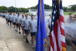 U.S. Airmen march by a U.S. flag and an Air Force flag.