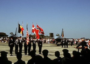 U.S. Air Forces Gen. Billy Minter, U.S. Air Forces in Europe commander, speaks during a ceremony at Hahn Air Base, Germany, July 9, 1982, commemorating USAFE’s first F-16 Fighting Falcons becoming operational. Belgian, Dutch, Danish and Norwegian flags displayed during the ceremony highlight the multinational partnership behind the F-16 program.
